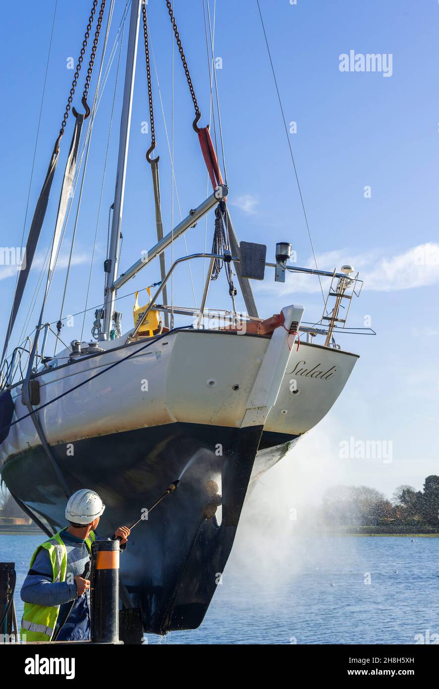 Craned out yacht, Contessa 26,in slings, the hull being pressure washed to remove weed at Bosham Quay, Chichester Harbour, West Sussex, England, UK Stock Photo