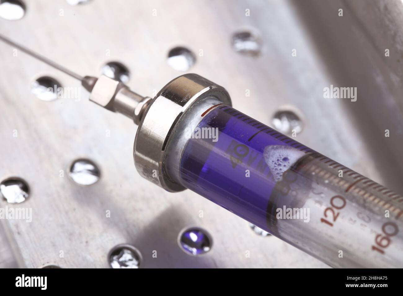 Obsolete syringe filled with blue solution ready for injecting. Stock Photo