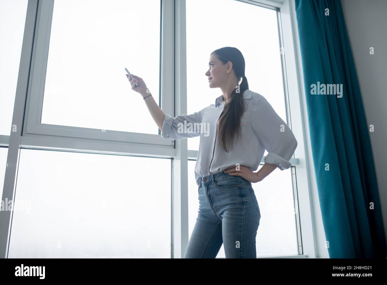 Concentrated lady using a remote control for closing the blinds Stock Photo