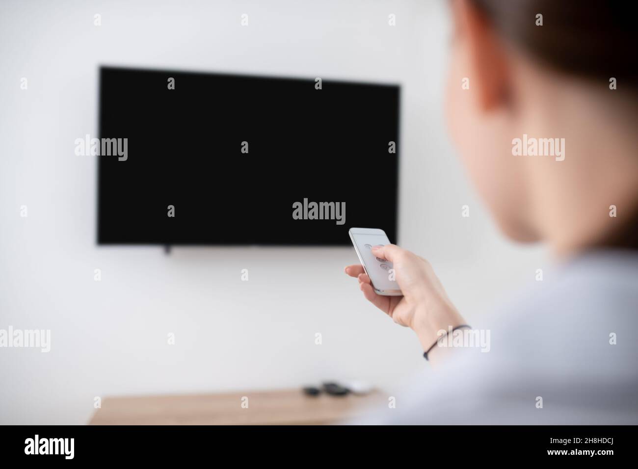 Female turning on the wall-mounted plasma TV Stock Photo