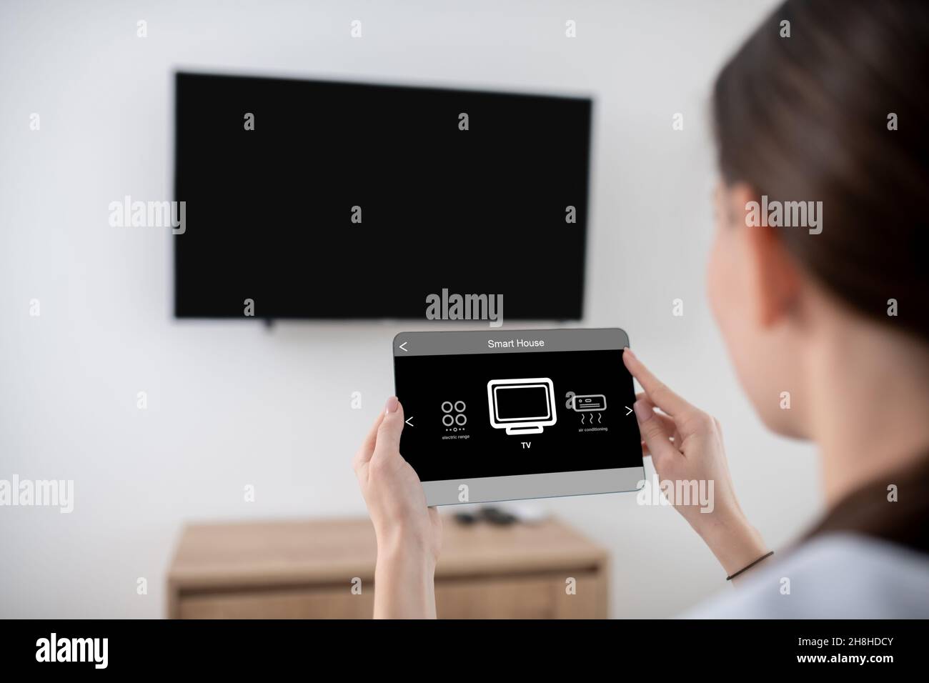 Woman turning on the flat screen television using a tablet Stock Photo