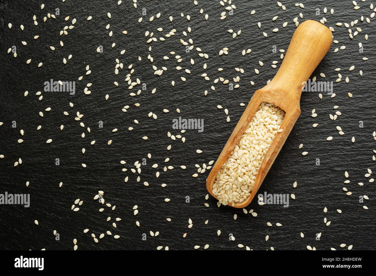 Organic natural sesame seeds on wooden spoon on slate background. Stock Photo