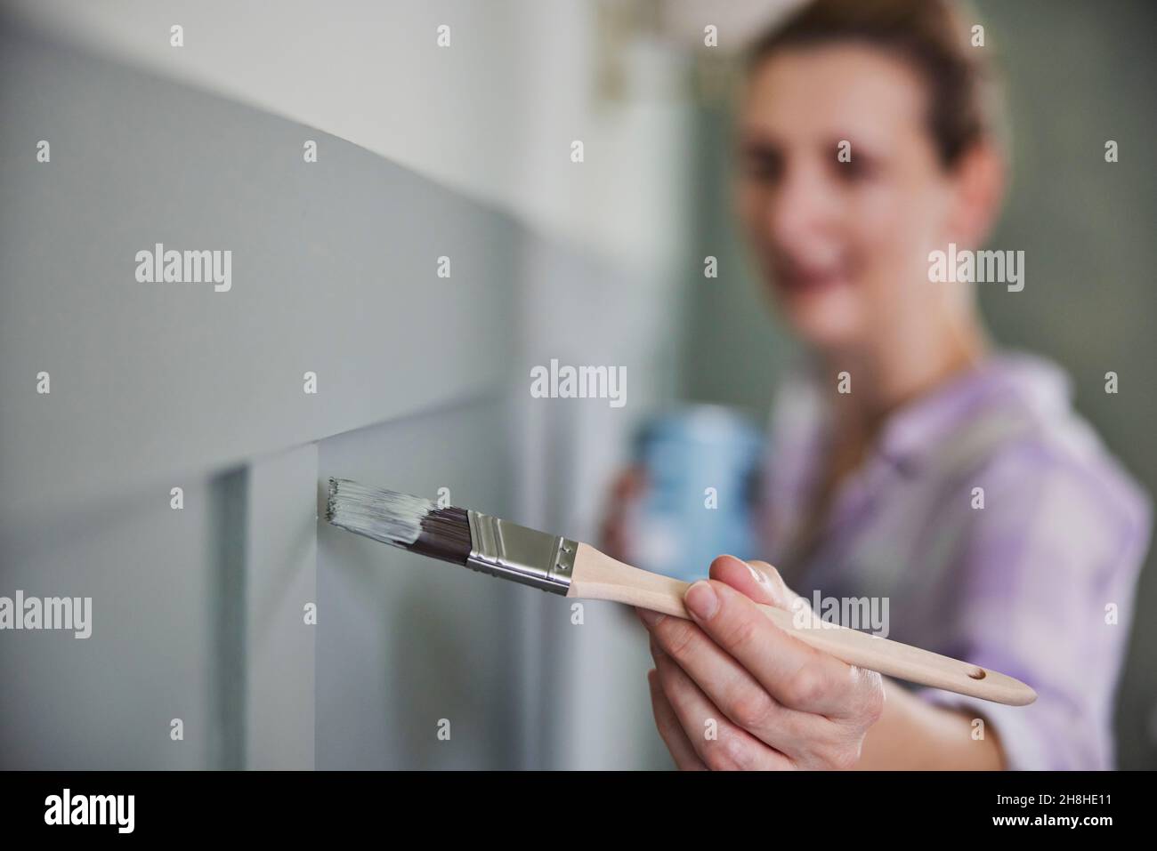 Woman Painting Wall With Panelling In Room Of House With Paint Brush Stock Photo