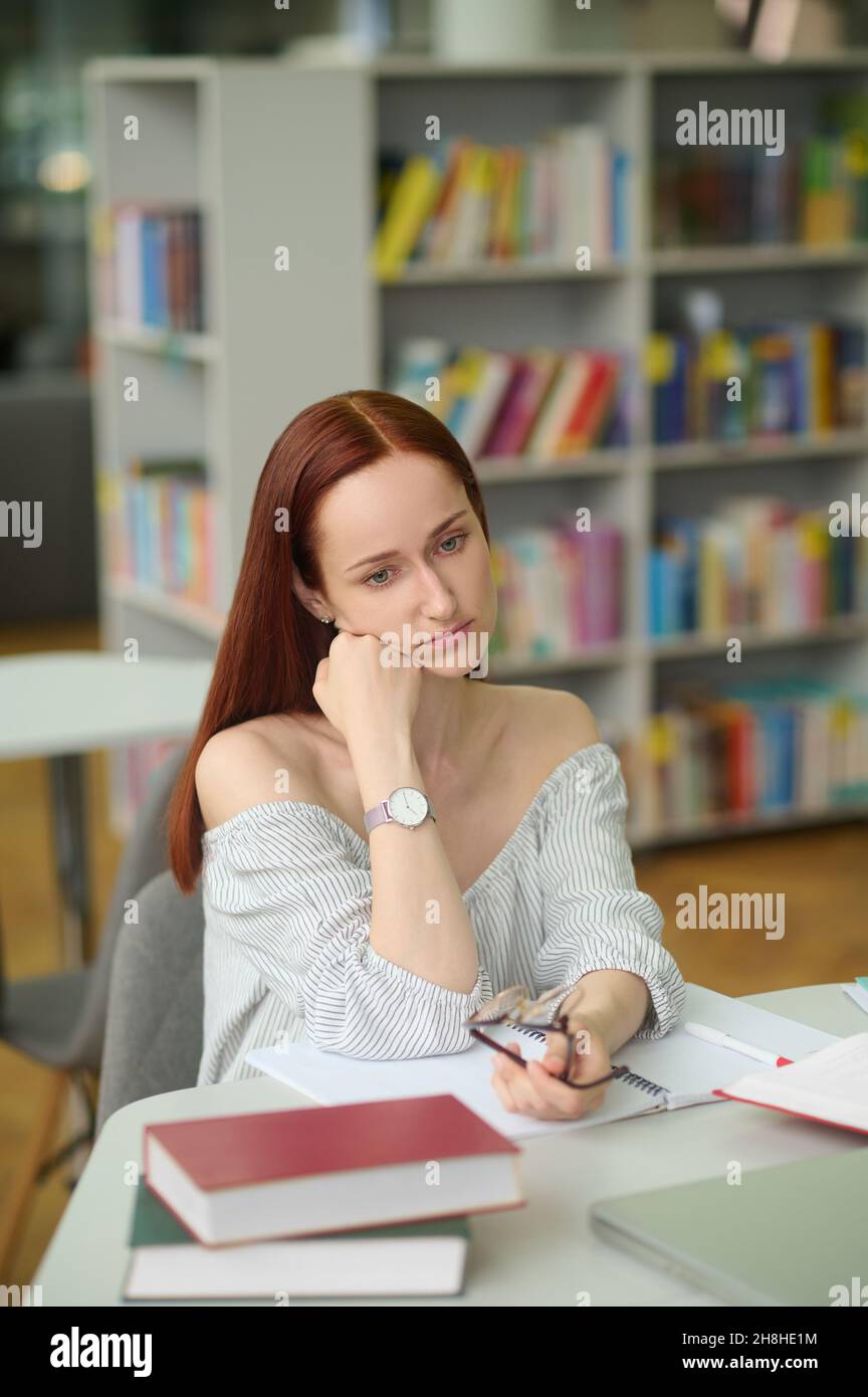 Pensive woman sitting at table in library Stock Photo
