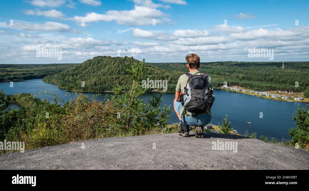 Young male backpacker squatting on a rock and enjoying the beautiful panoramic landscape. Stock Photo