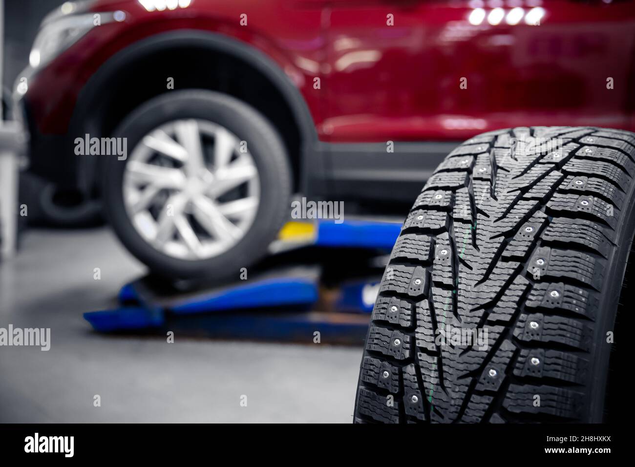Selective focus winter tire with steel studs in service, in background car is lifted on lift. Stock Photo