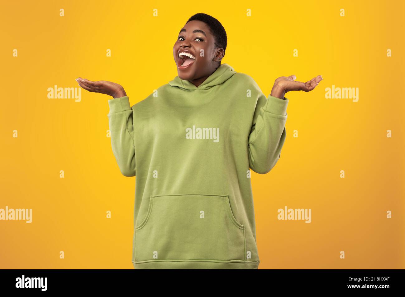 Cheerful Black Overweight Lady Shrugging Shoulders Posing On Yellow Background Stock Photo