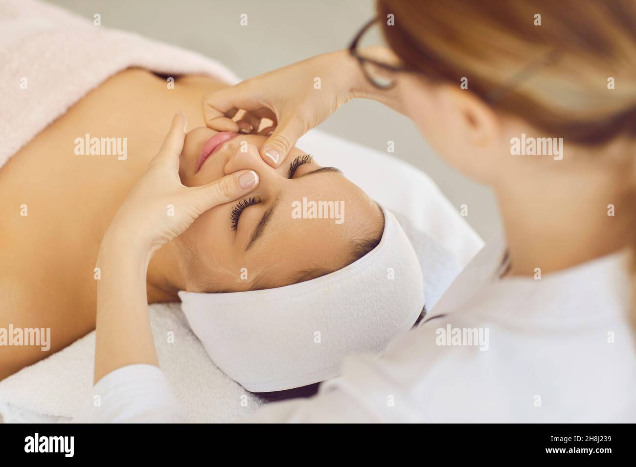 Female beautician doing facial massage for client lying in beauty center or spa. Stock Photo