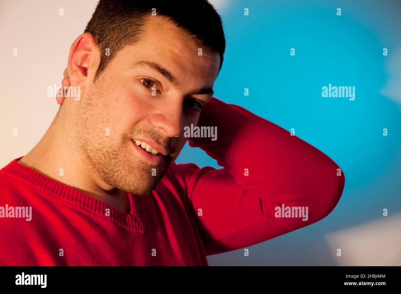 Young man, hand on head, looking camera. Close view. Stock Photo