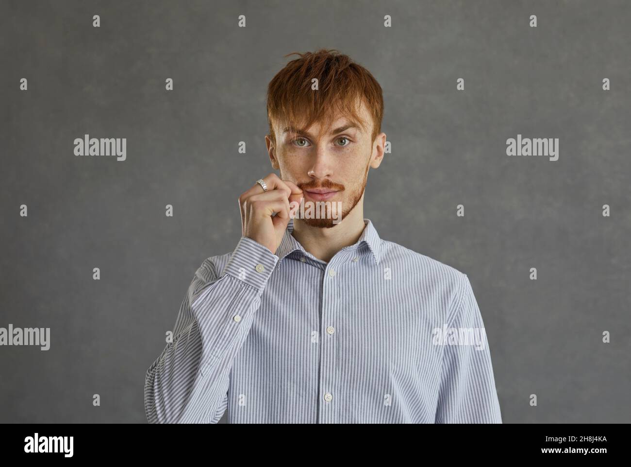 Casual red-haired man showing mouth with zipper secret sign studio shot Stock Photo