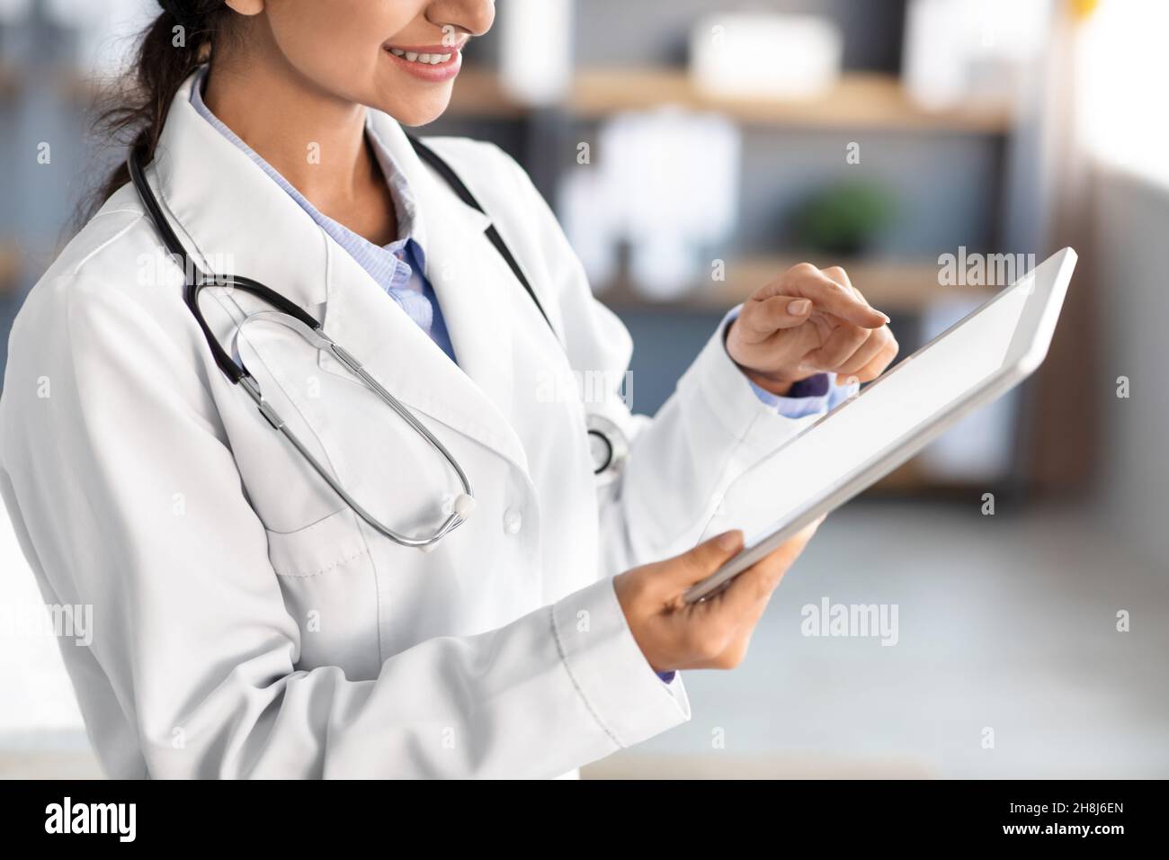 Cropped smiling young pretty indian woman doctor in white coat examines ...