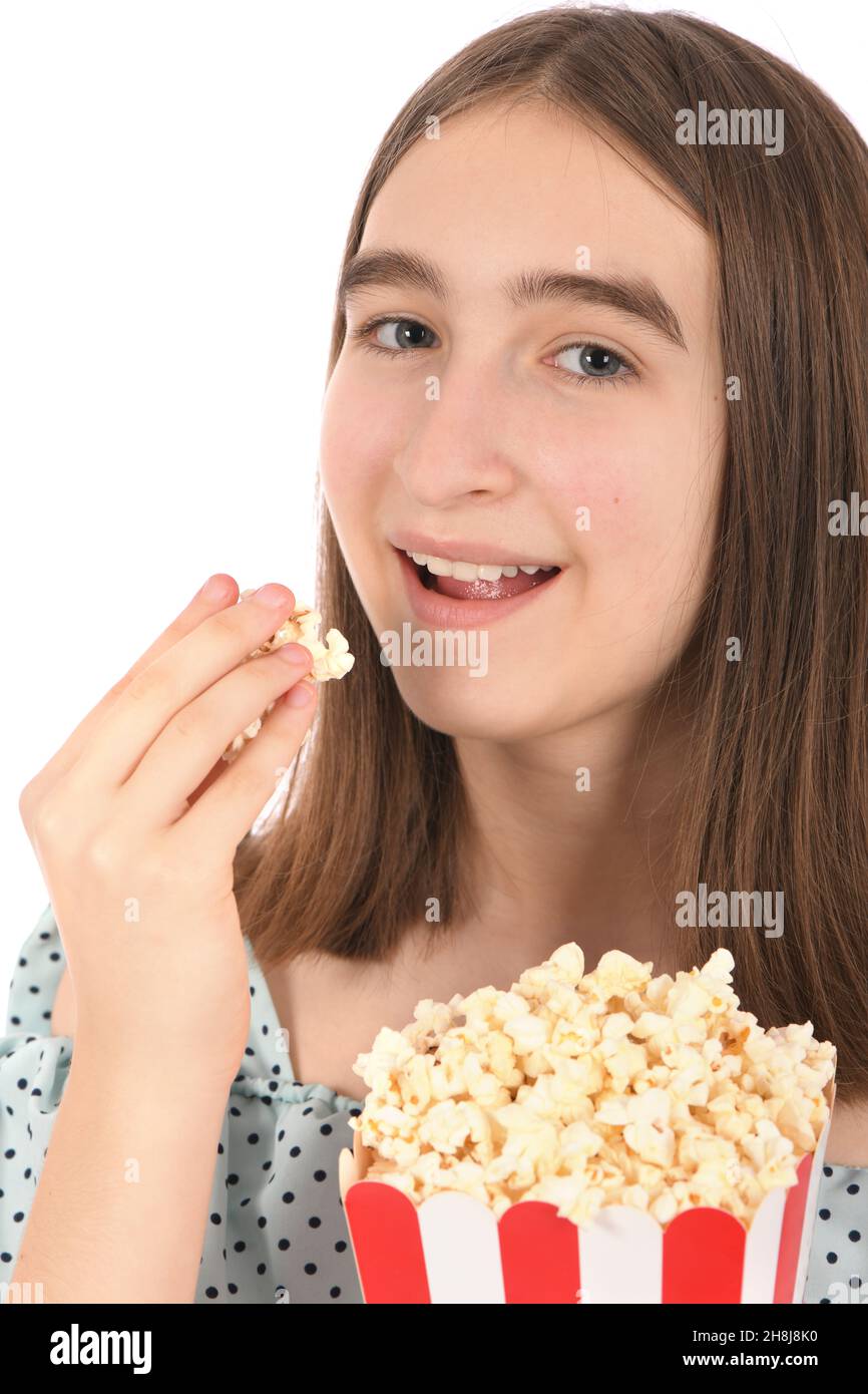 Teenage girl eating popcorn, standing on white. High resolution photo