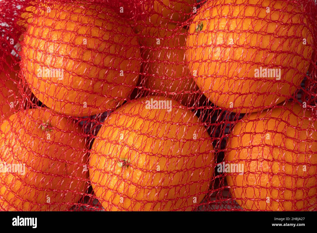 Fresh oranges in plastic mesh from supermarket Stock Photo