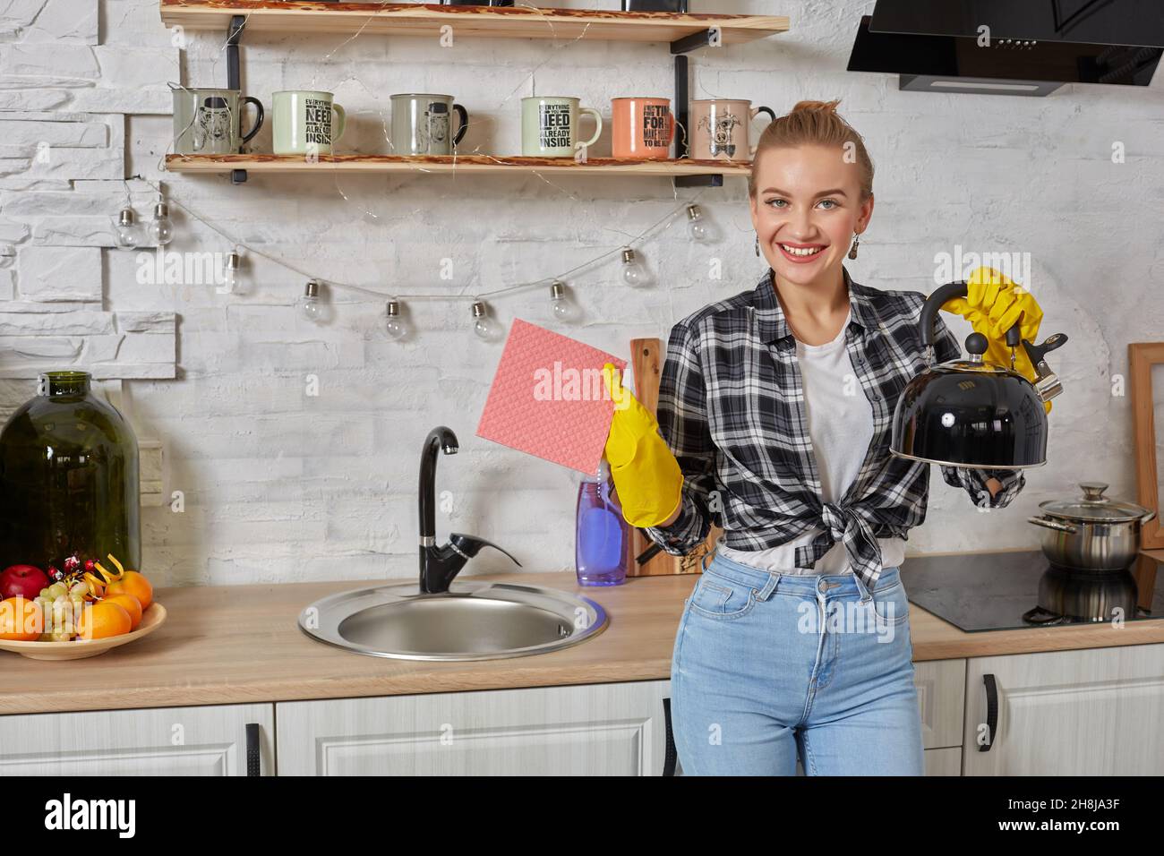 Domestic service and housekeeping concept, happy blonde lady cleaning kitchen kettle. Stock Photo