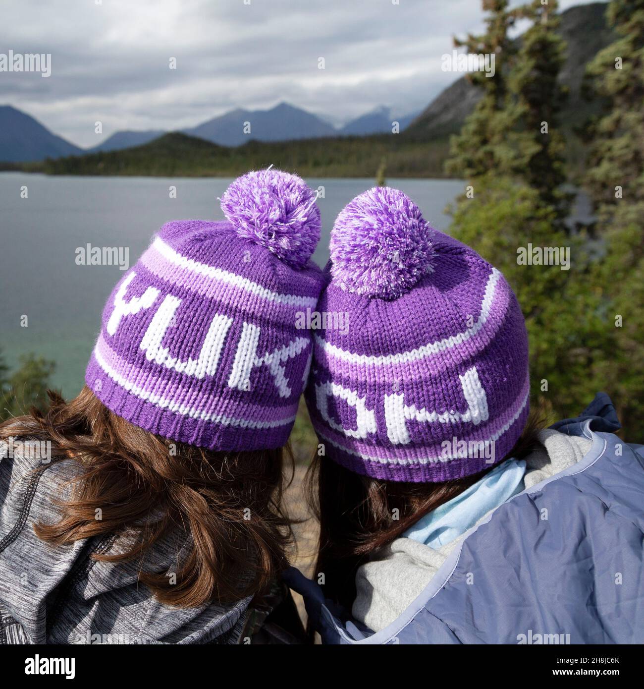 People wearing Yukon bobble hats, known as toquesin the Yukon, Canada. They look outonto one of the territory's lakes. Stock Photo