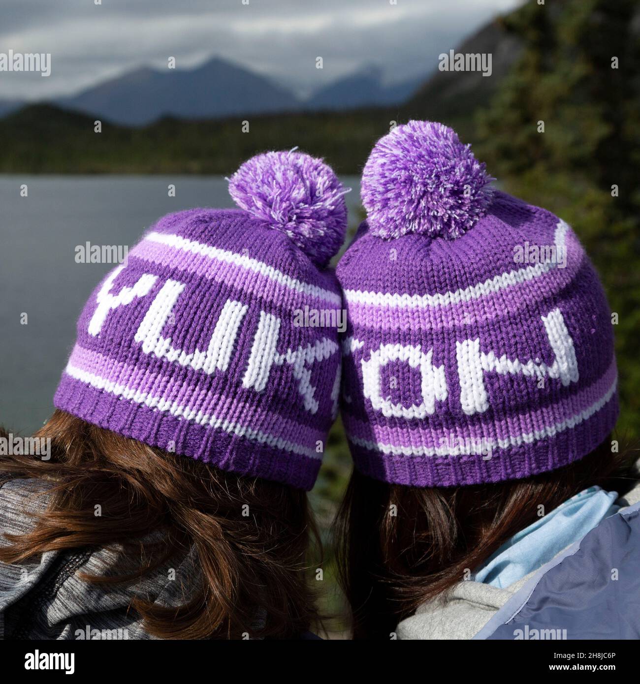People wearing Yukon bobble hats, known as toquesin the Yukon, Canada. They look outonto one of the territory's lakes. Stock Photo