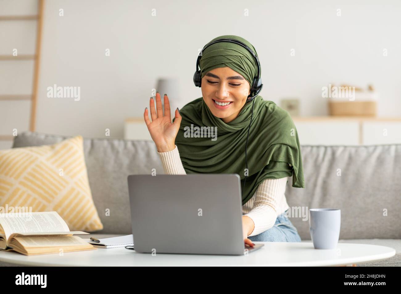 Happy young Arab lady in hijab and headset making video call on laptop at  home, waving at screen Stock Photo - Alamy