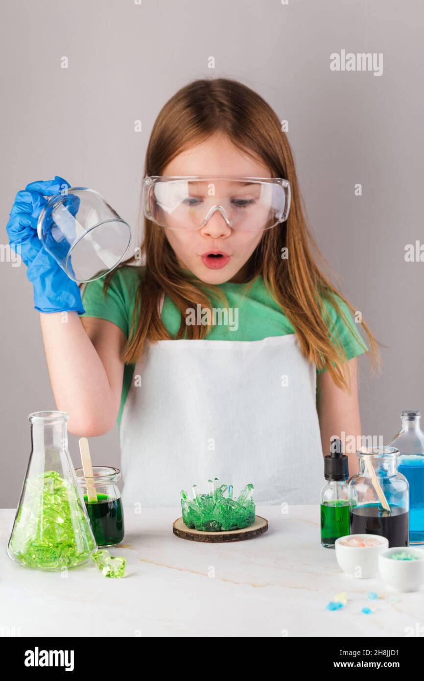 Cute girl in chemistry glasses impressed by green crystal growth