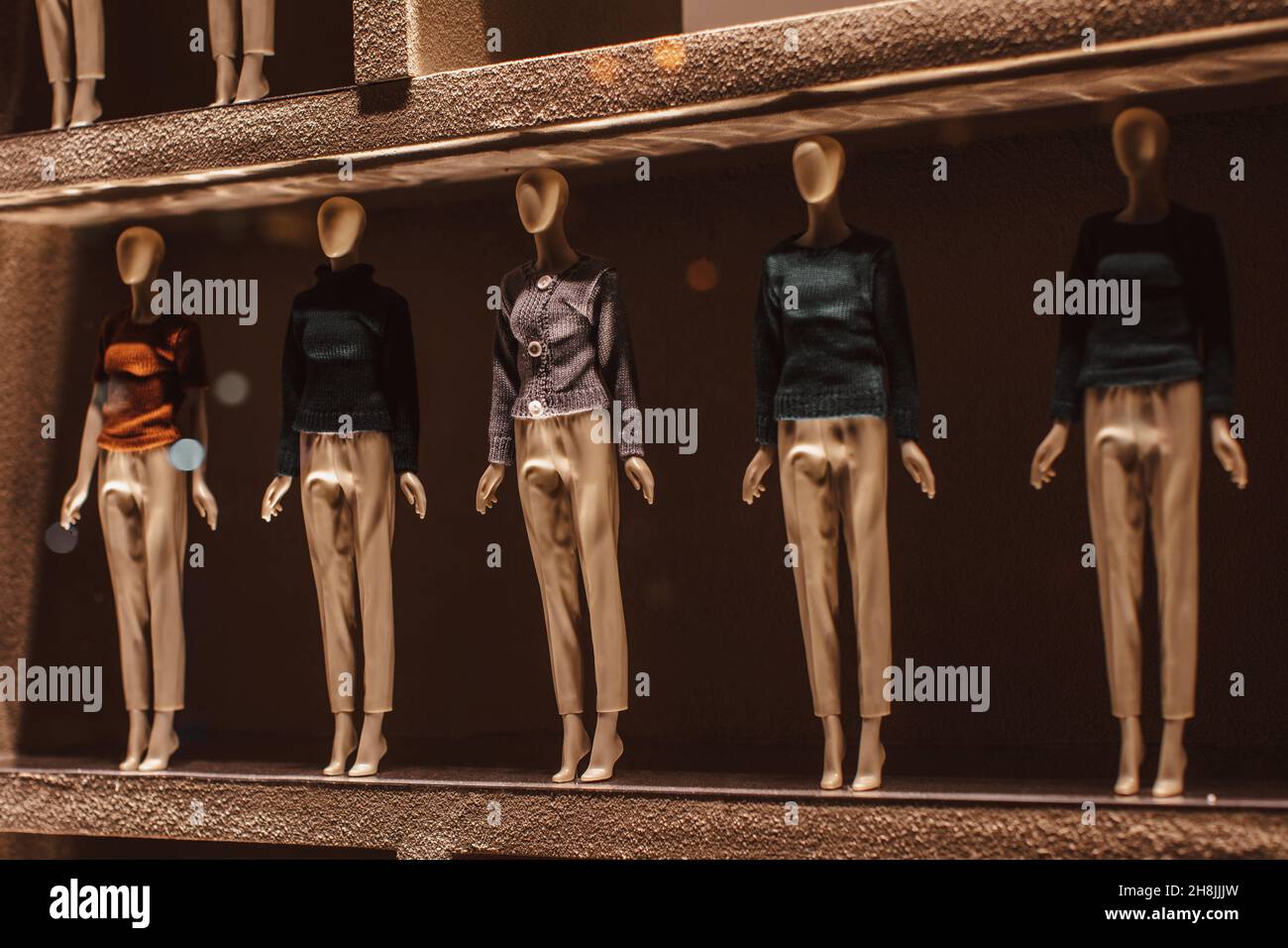 Tiny dolls, mannequins dressed in warm knitted sweaters and beige trousers. Autumn winter fashion collection at the display window. Stock Photo