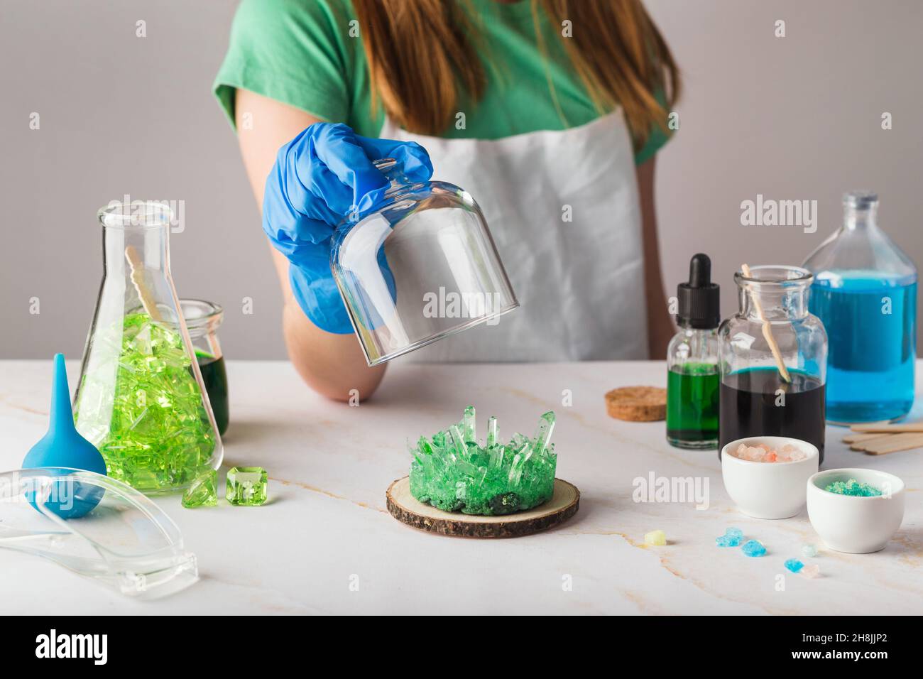 Cute girl in chemistry glasses impressed by green crystal growth