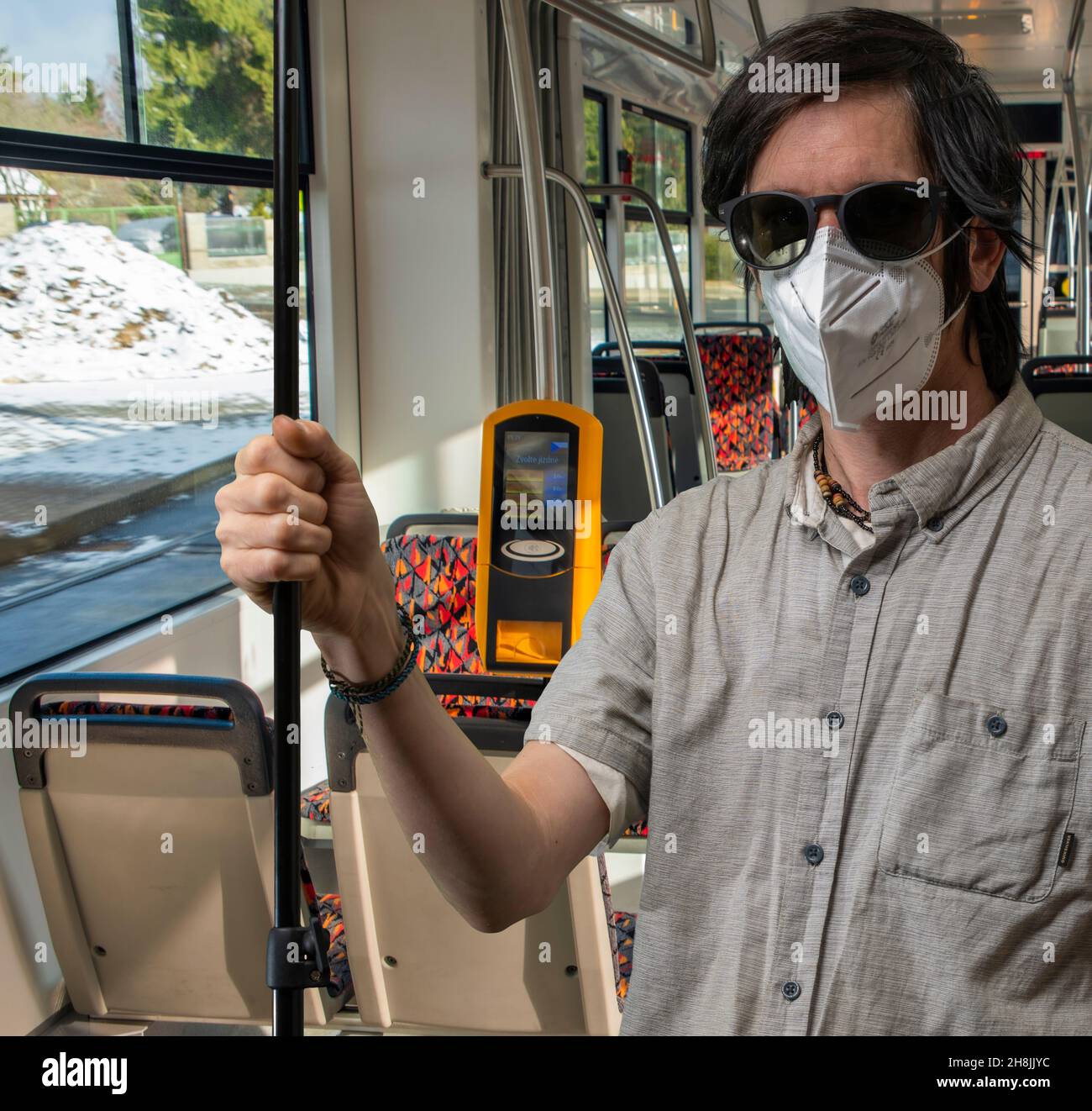 Black hair man with respirator and grey shirt in streetcar in winter sunny day Stock Photo