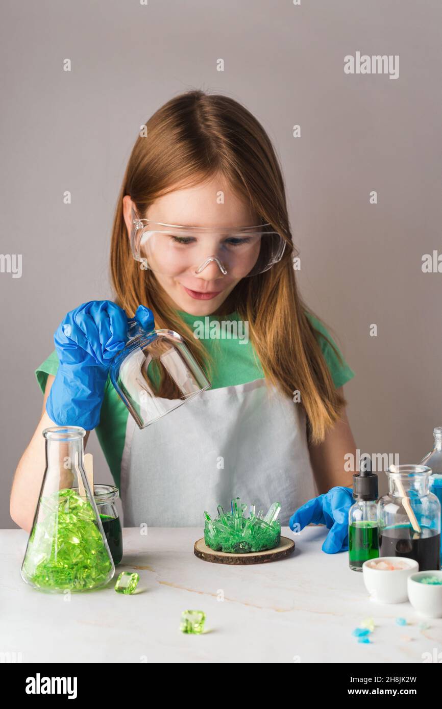 Cute girl in chemistry glasses impressed by green crystal growth