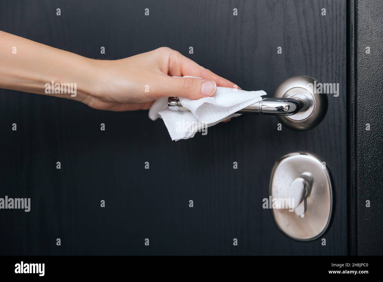 Cleaning black door handles with an antiseptic wet wipe. Woman hand