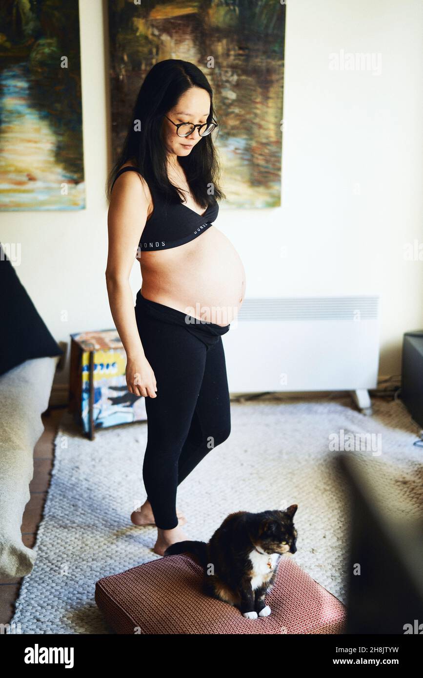 Pregnant woman in sports bra, with cat in living room Stock Photo