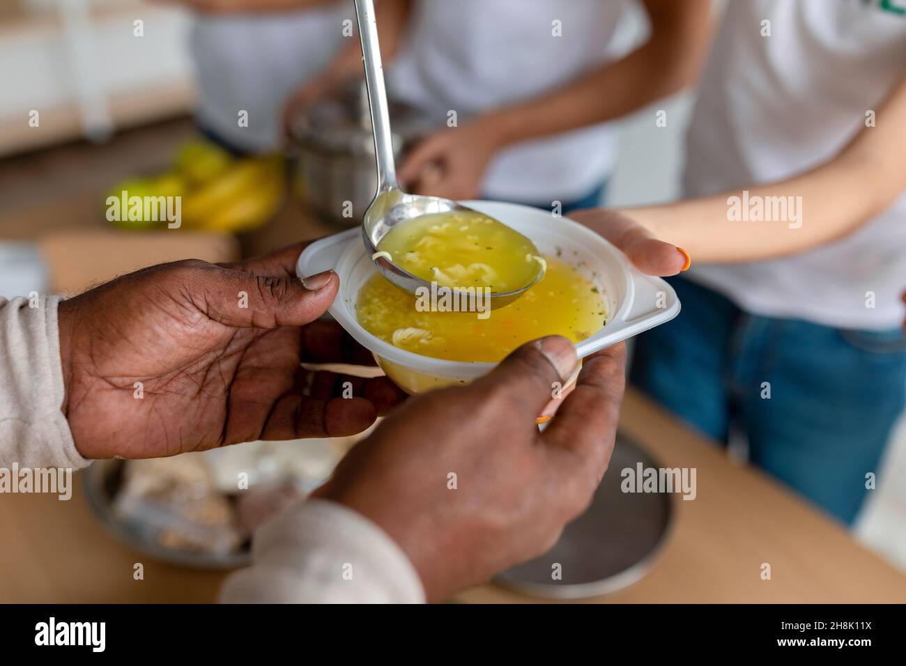 Volunteers help. Young people serving hot soup for homeless in community charity donation center, closeup Stock Photo