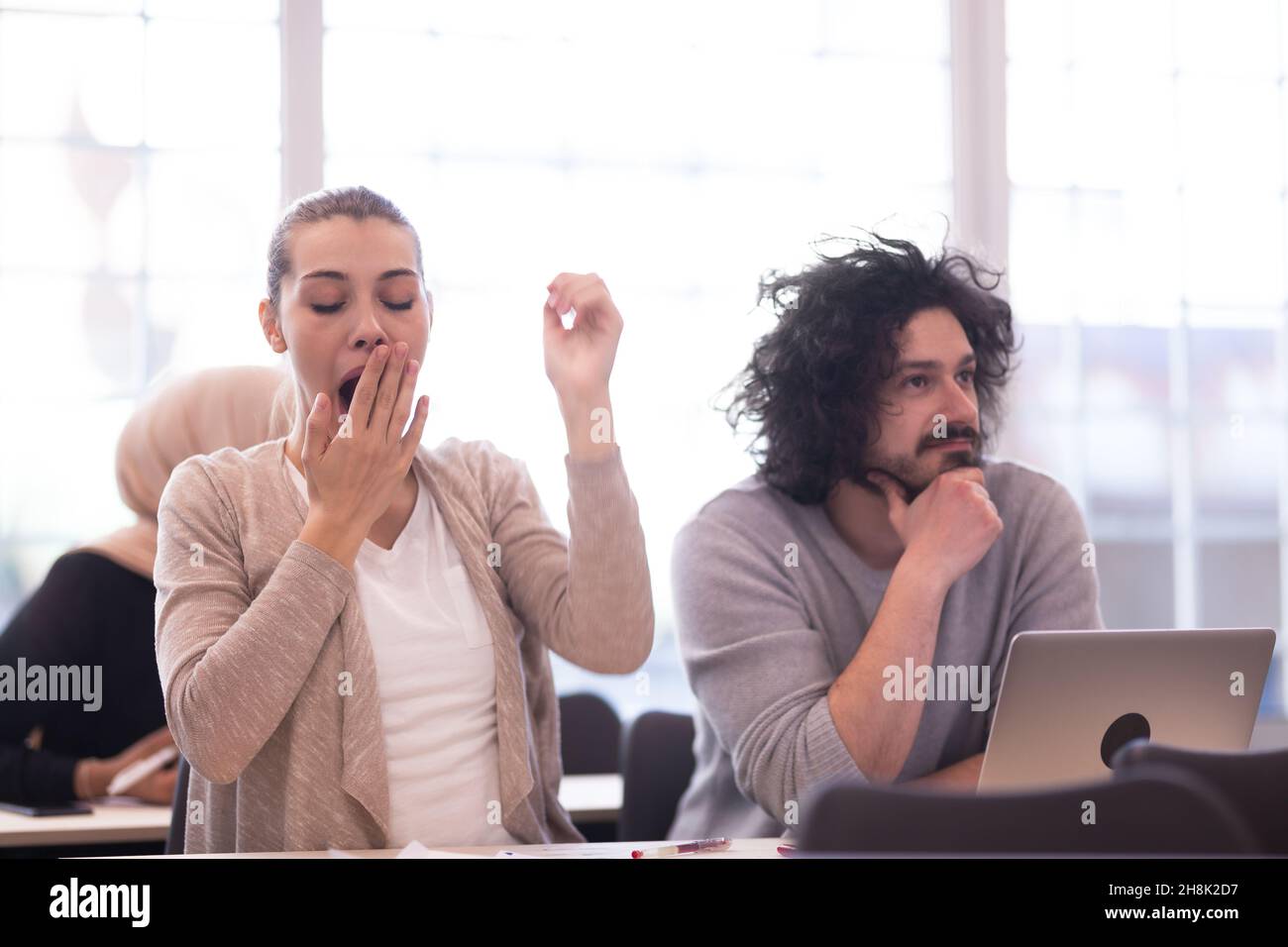 Students listening to a lecturer in a classroom. Smart young girl yawning during class. Stock Photo