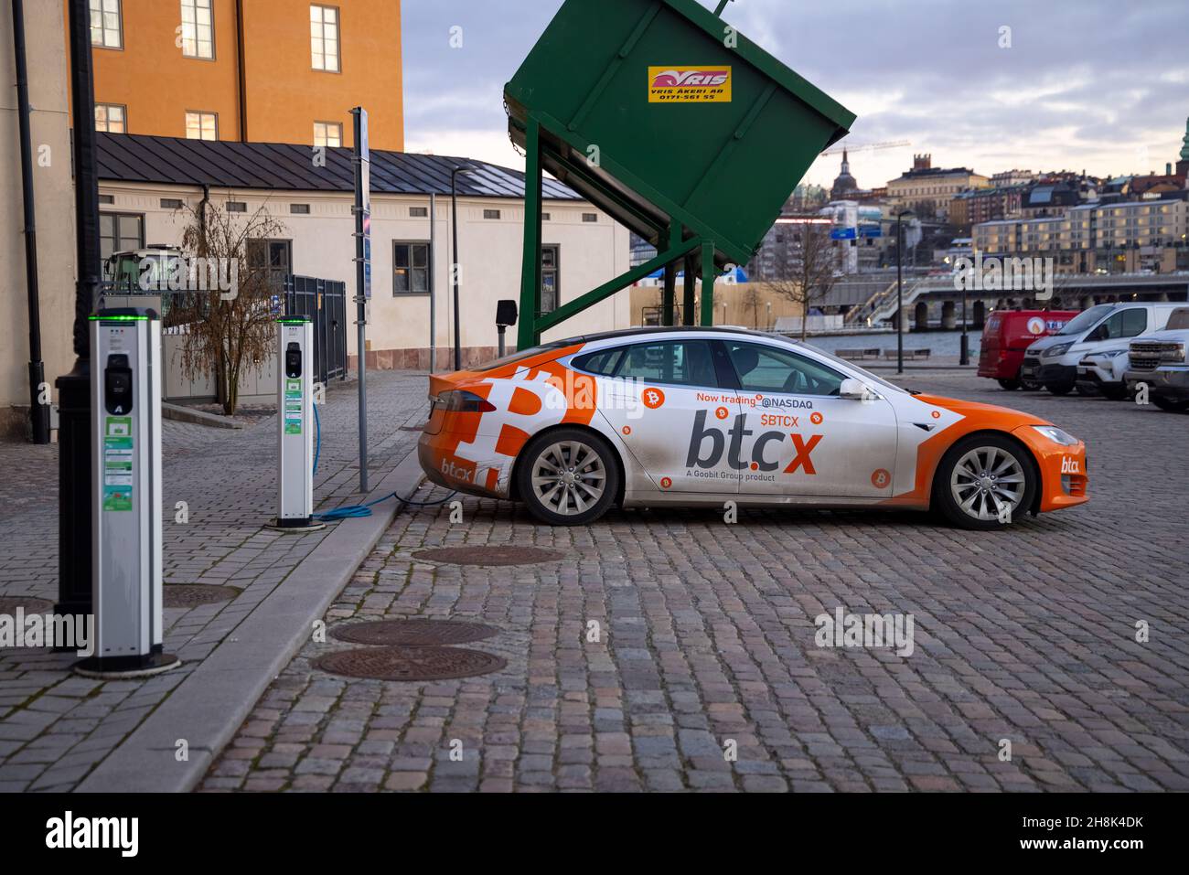 Electric car charging point with Tesla car plugged in decorated with Bitcoin  and Nasdaq logotypes and plate. Bitcoin and cryptocurrency advertising  Stock Photo - Alamy