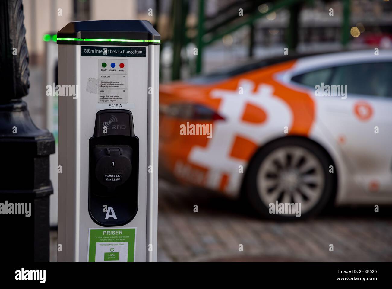 Electric car charging point with Tesla car plugged in decorated with Bitcoin  and Nasdaq logotypes and plate. Bitcoin and cryptocurrency advertising  Stock Photo - Alamy