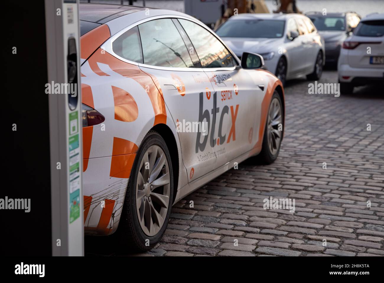 Electric car charging point with Tesla car plugged in decorated with Bitcoin  and Nasdaq logotypes and plate. Bitcoin and cryptocurrency advertising  Stock Photo - Alamy