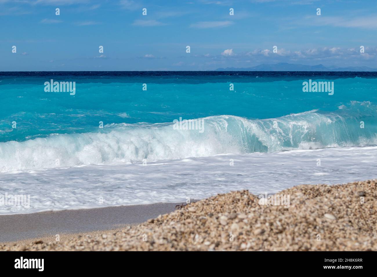 Azure vibrant breaker waves hitting pebble shore. Sunny coast of Greek island with blue sky. Sandy beach in Greece. Summer nature travel to Ionian Sea Stock Photo