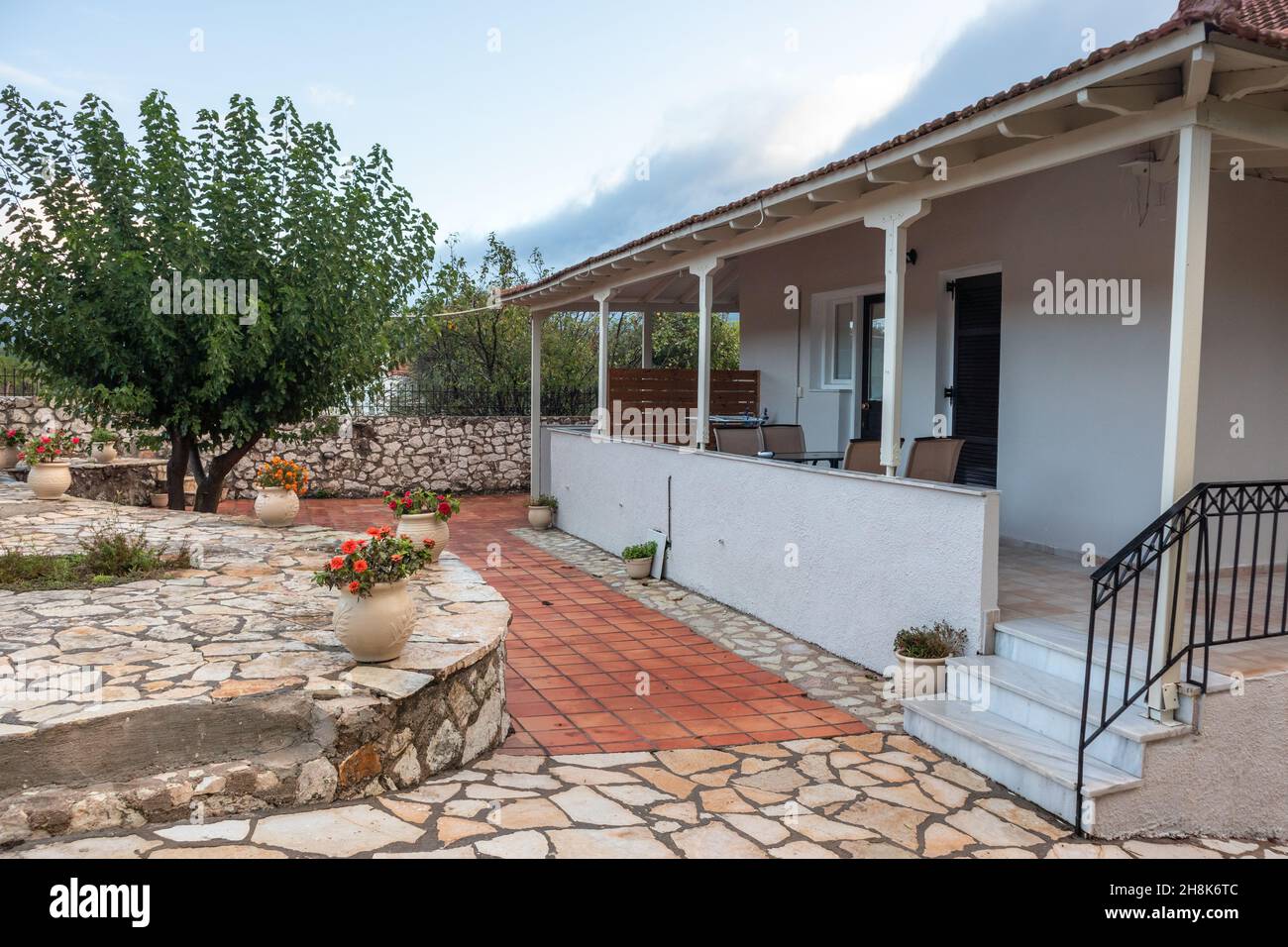 Greek village traditional villa with stone decor, red tiling, flower pots and green trees. Summer travel in Mediterranean Stock Photo