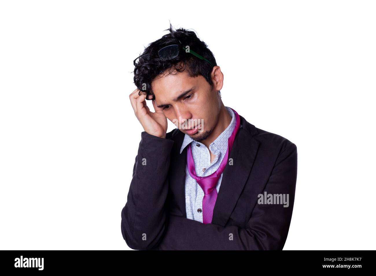 Businessman with a disheveled tie and deep in thought scratches his head while looking down. Young adult businessman isolated on all white background. Stock Photo