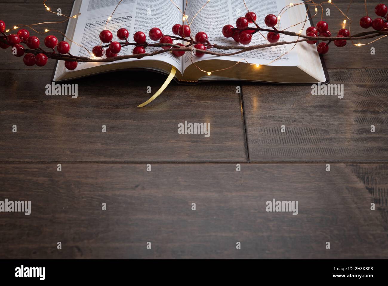 Red berry garland and string of mini fairy christmas lights on an open bible on a dark wood background with copy space Stock Photo