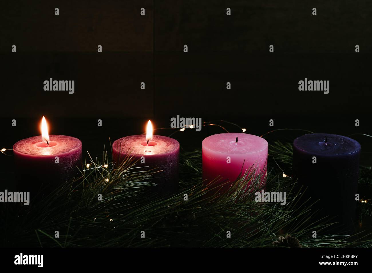 Two pillar candles lit on an advent wreath in a dark room for the second week of advent with