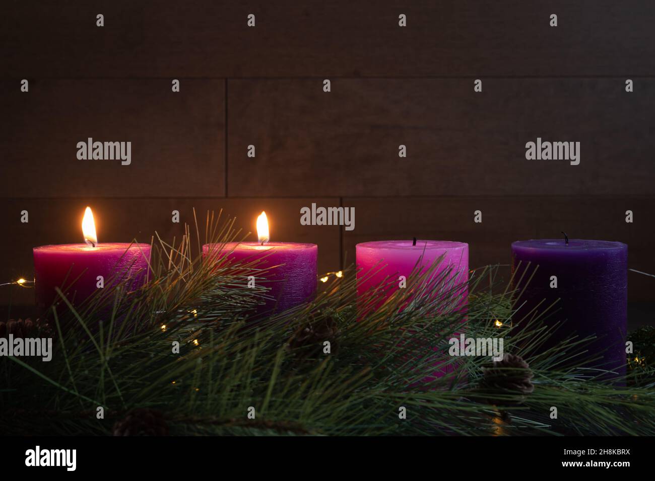 Two pillar candles lit on an advent wreath in a dark room for the second week of advent with