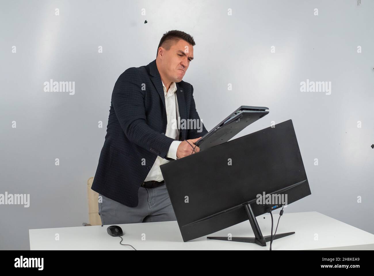 Caucasian man in a suit gets angry and smashes the keyboard on the monitor. An office worker in a rage breaks the computer. Stock Photo
