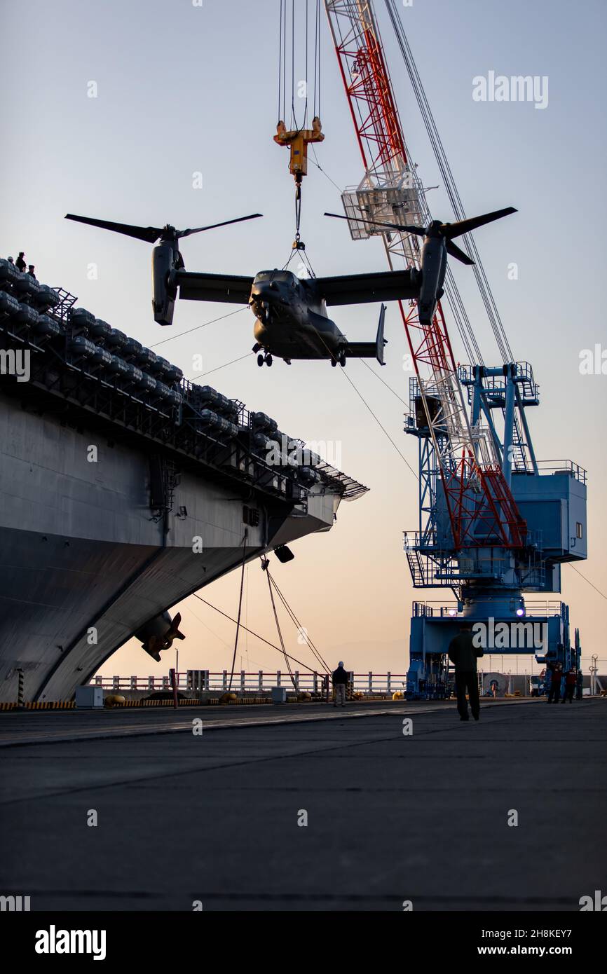 A CV-22 Osprey aircraft is craned off of the USS America (LHA 6) onto Marine Corps Air Station Iwakuni, Japan’s flight line,  Nov. 20, 2021. Due to its geographic location and co-located airfield and harbor, the air station is uniquely postured to provide advanced naval integration in support of regional security. (U. S. Marine Corps photo by Cpl. Phuchung Nguyen). Stock Photo