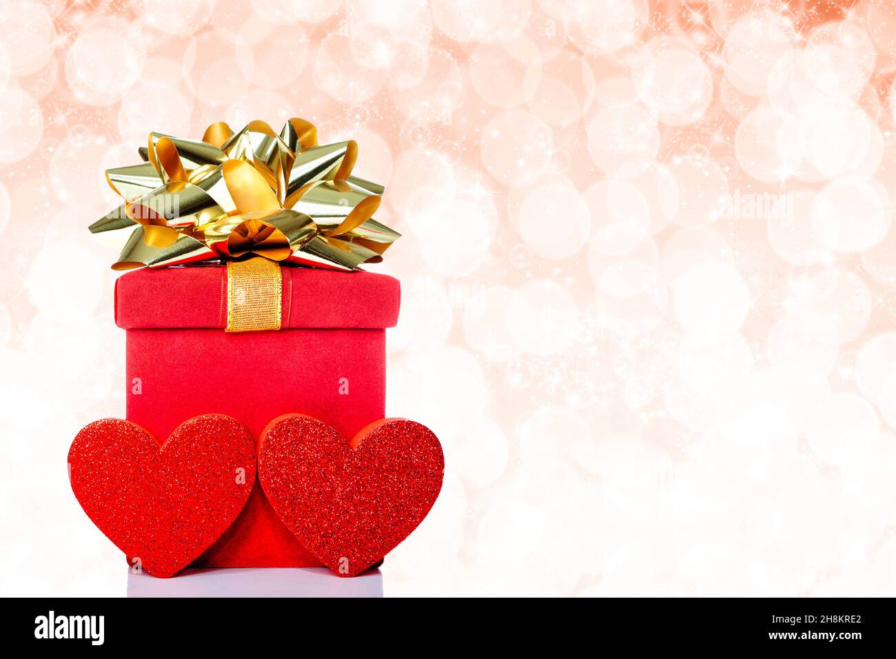 Red gift box with golden bow and hearts on glittering background with ...
