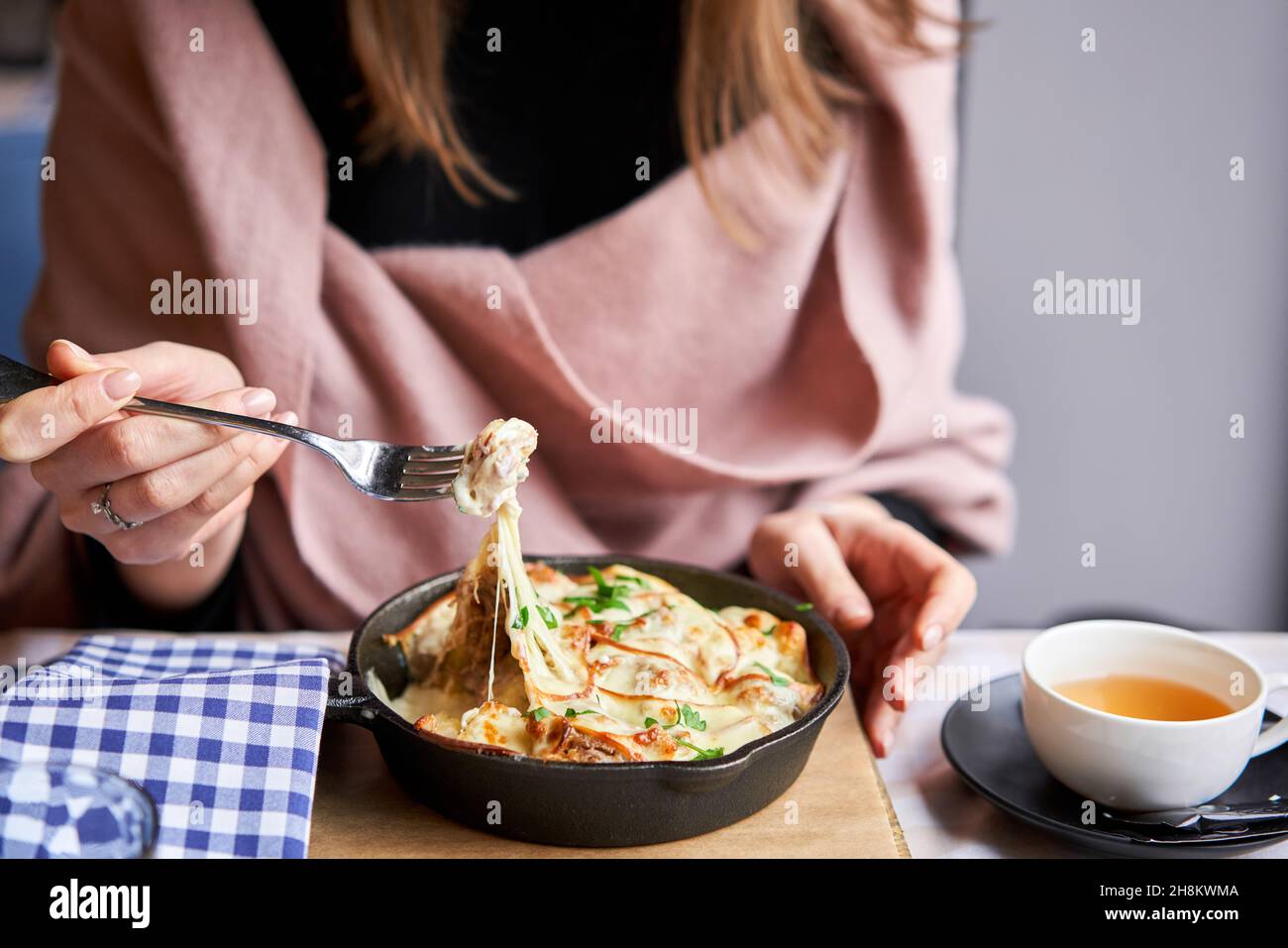 Potato with cheese casserole in a cast-iron frying pan. Close-up of a woman eating with a fork. Latvian cuisine. Stock Photo