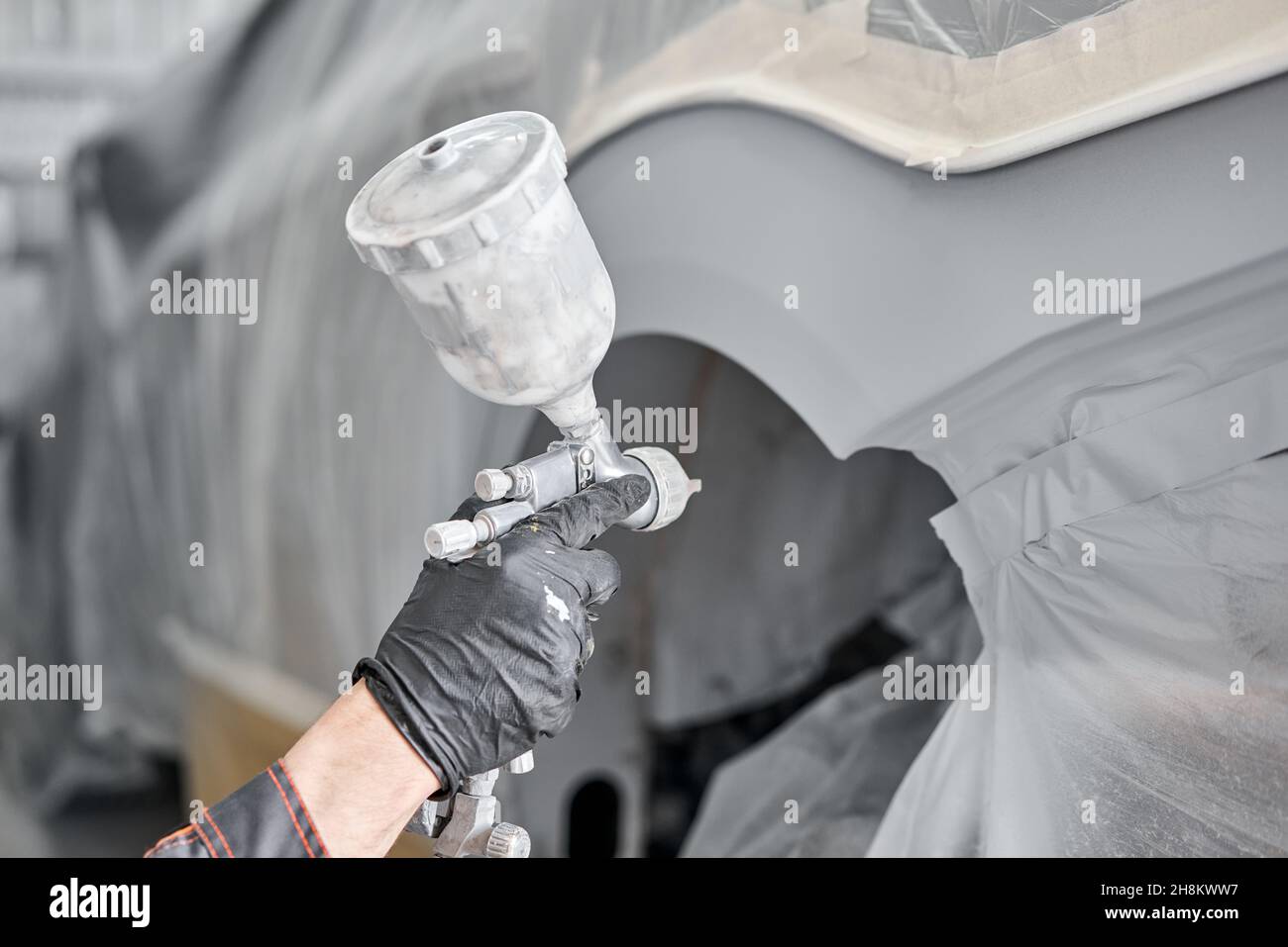 Painting the rear part of the car. Car painter wearing costume and protective gear. Car service station. Restoring a car after an accident. Stock Photo