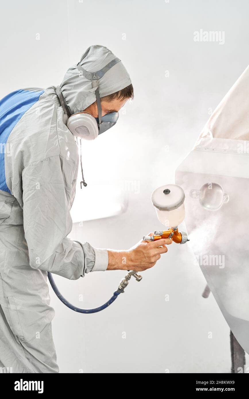 Painting the rear door of the car. Car painter in special painting chamber, wearing costume and protective gear. Car service station. Restoring a car Stock Photo
