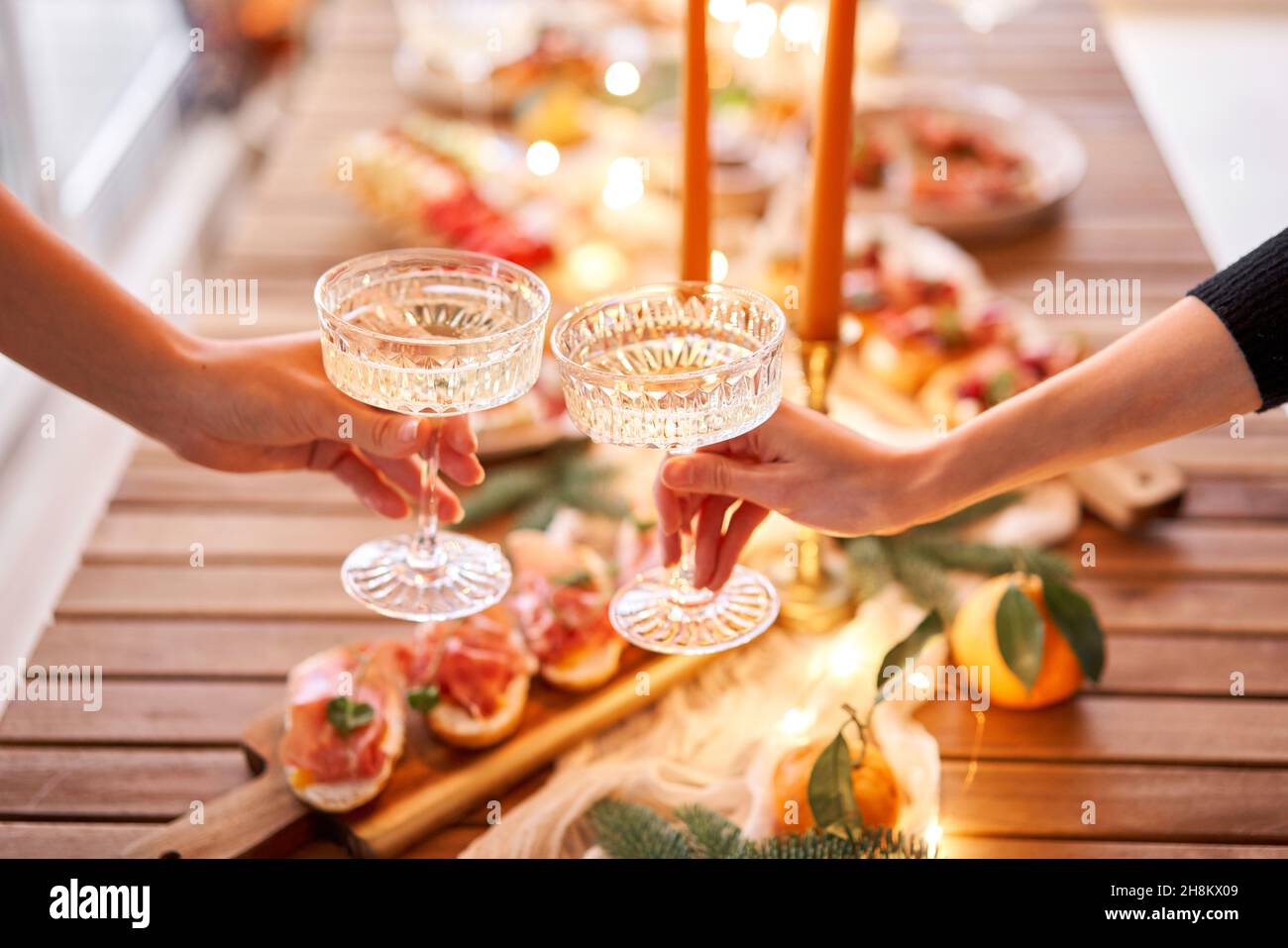 Christmas dinner feast. A small table is served with snacks, bruschettas, and canapes. A decorated dining table with champagne glasses, candles and ch Stock Photo
