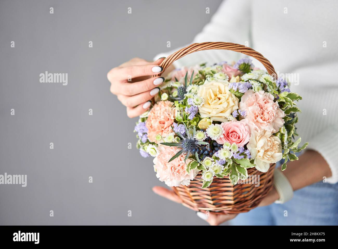 Flower arrangement in Wicker basket. Beautiful bouquet of mixed flowers in woman hand. Handsome fresh bouquet. Small flower shop and Flowers delivery Stock Photo
