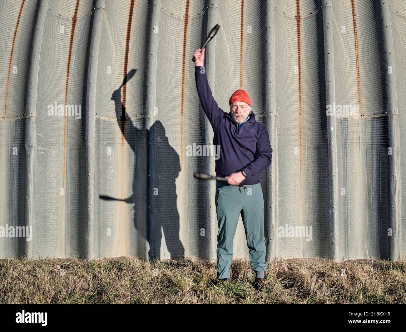 senior athletic male is exercising with Indian clubs with a company of a shadow on a grunge metal hangar, workout in urban or industrial environment Stock Photo