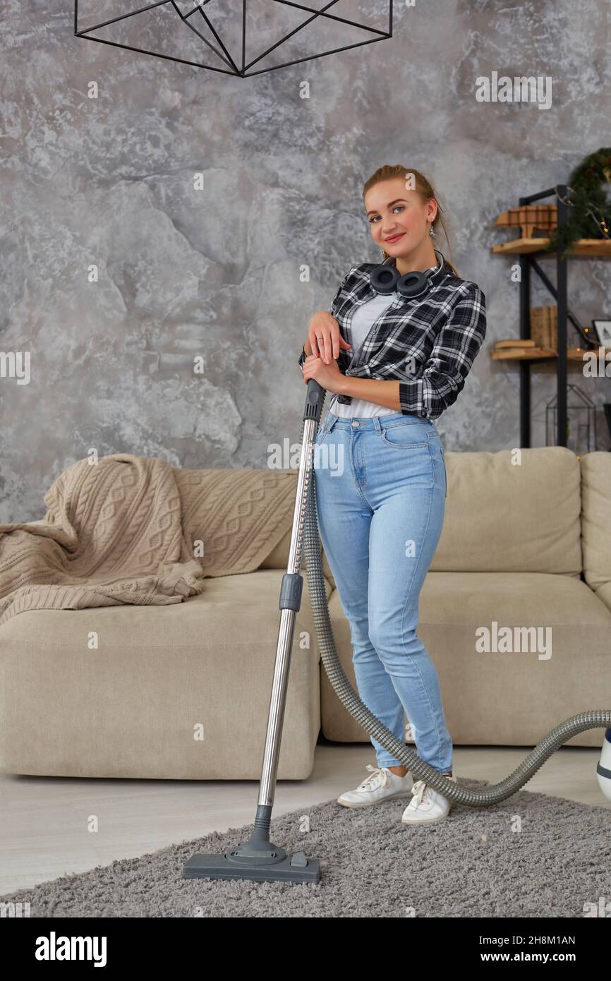 Young smiling woman vacuum cleaning the carpet in the living room ...