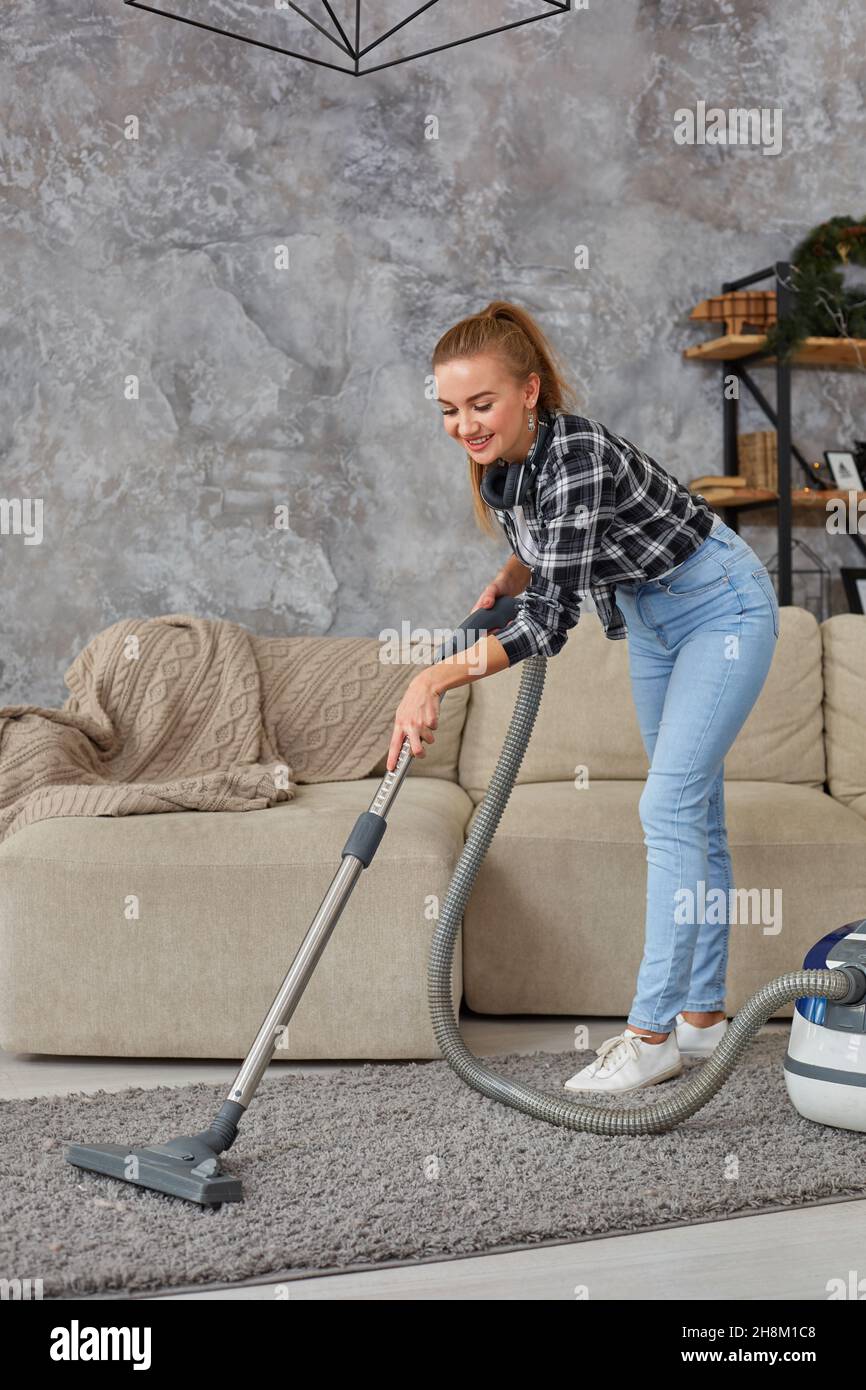 Young smiling woman vacuum cleaning the carpet in the living room ...